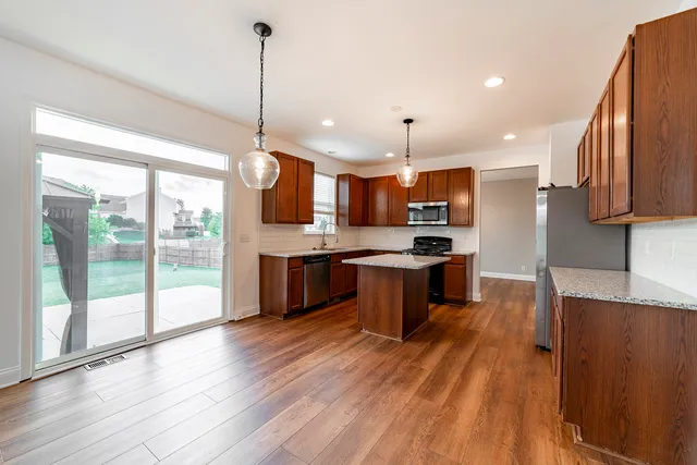 a kitchen with stainless steel appliances kitchen island granite countertop a stove a sink a refrigerator a center island with wooden floor and cabinets