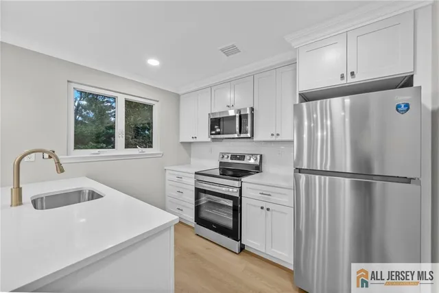 a white kitchen with sink a refrigerator and a stove top oven