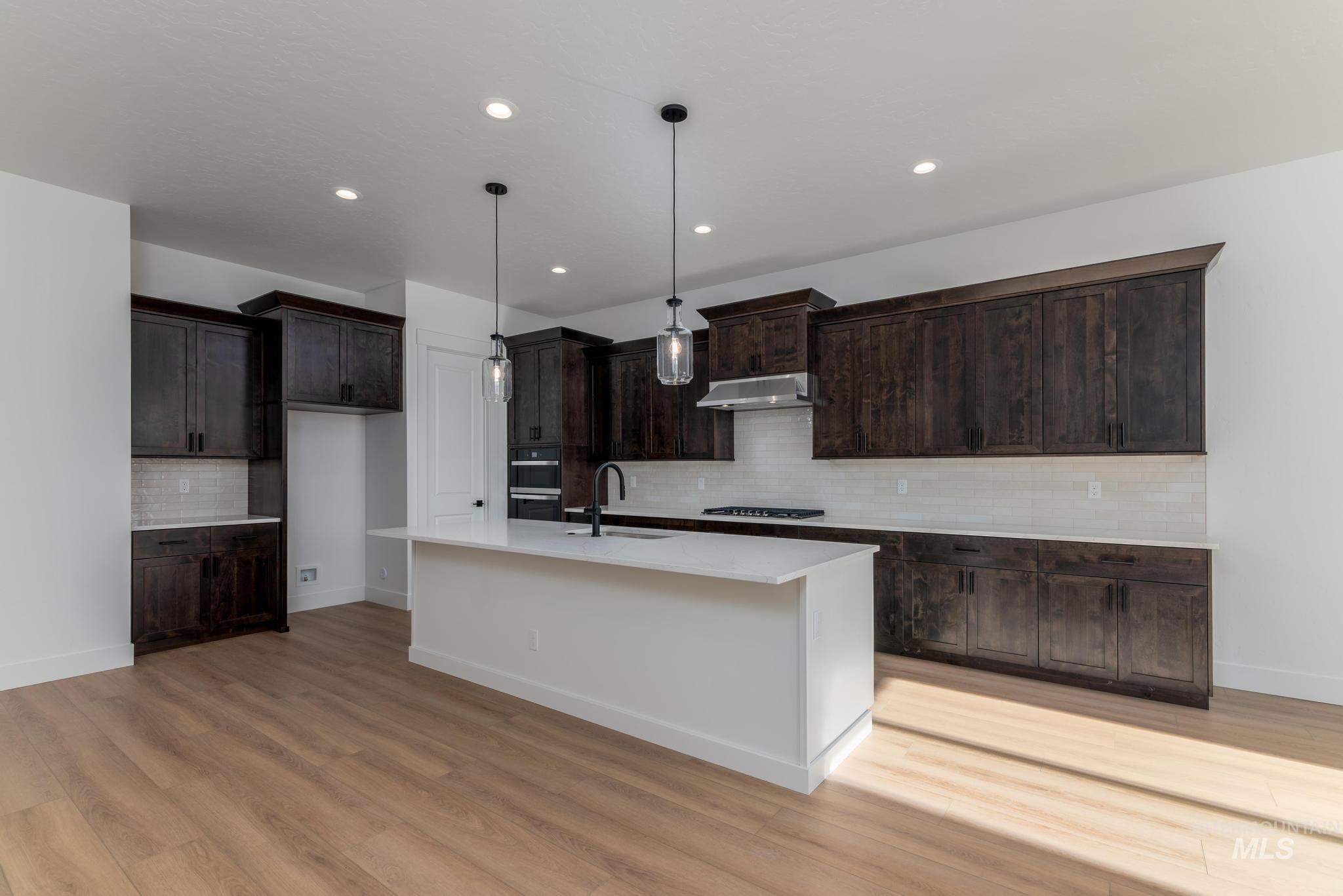 9085 West Patmore Court Star, ID 83669 - Photo 10 of 40 Kitchen with hanging light fixtures, decorative backsplash, dark brown cabinetry, a center island with sink, and light wood-type flooring