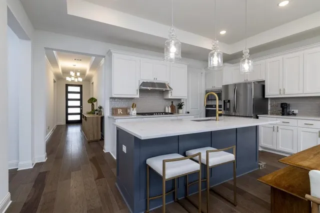 a kitchen with kitchen island granite countertop a view of a sink a stove a refrigerator and chairs