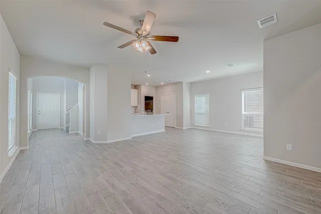 an empty room with wooden floor fan and windows