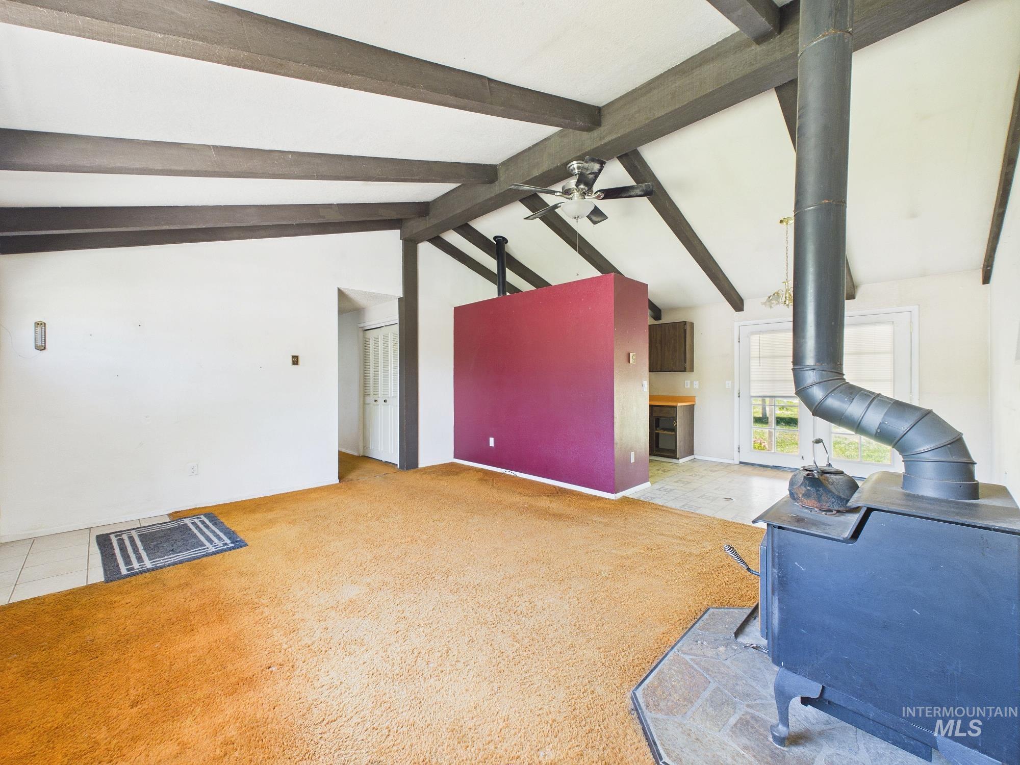 1527 North Plaza Road Emmett, ID 83617 - Photo 6 of 33 Vaulted ceiling with exposed wood beams, wood-burning stove with stone hearth, and a partial wall separating spaces