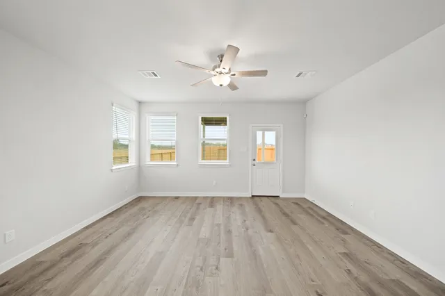 an empty room with wooden floor ceiling fan and windows