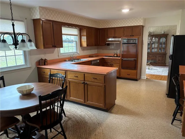 a kitchen with stainless steel appliances granite countertop a stove a refrigerator a sink dishwasher a dining table and chairs with wooden floor