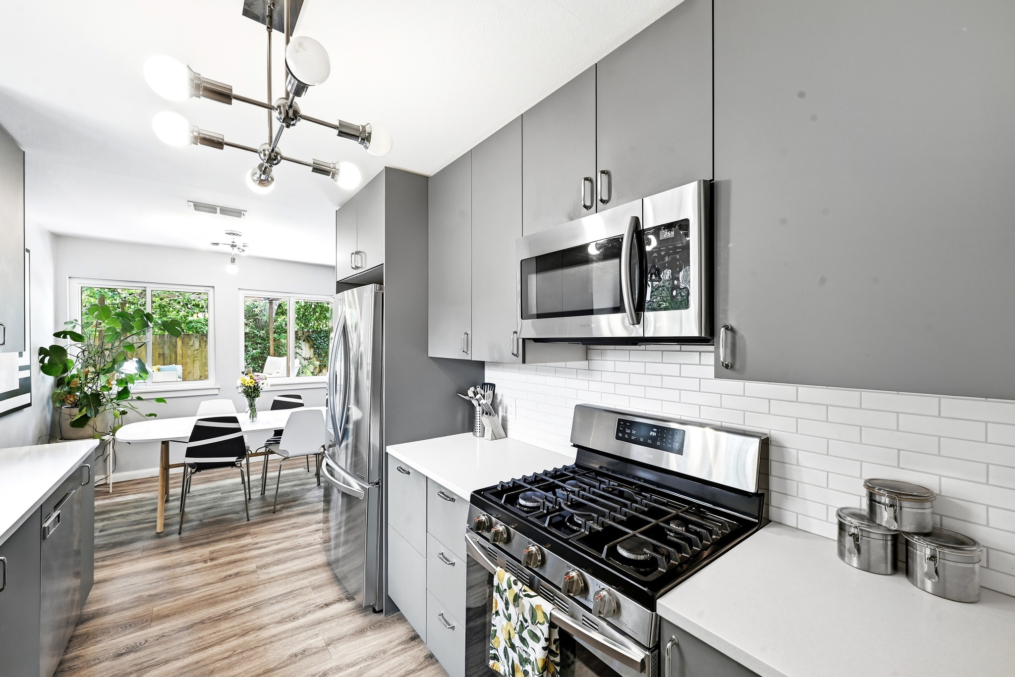 7110 Windrift Way Austin, TX 78745 - Photo 13 of 30 A well-lit kitchen boasts sleek gray cabinetry, stainless steel appliances, and a dining area with views of lush greenery.