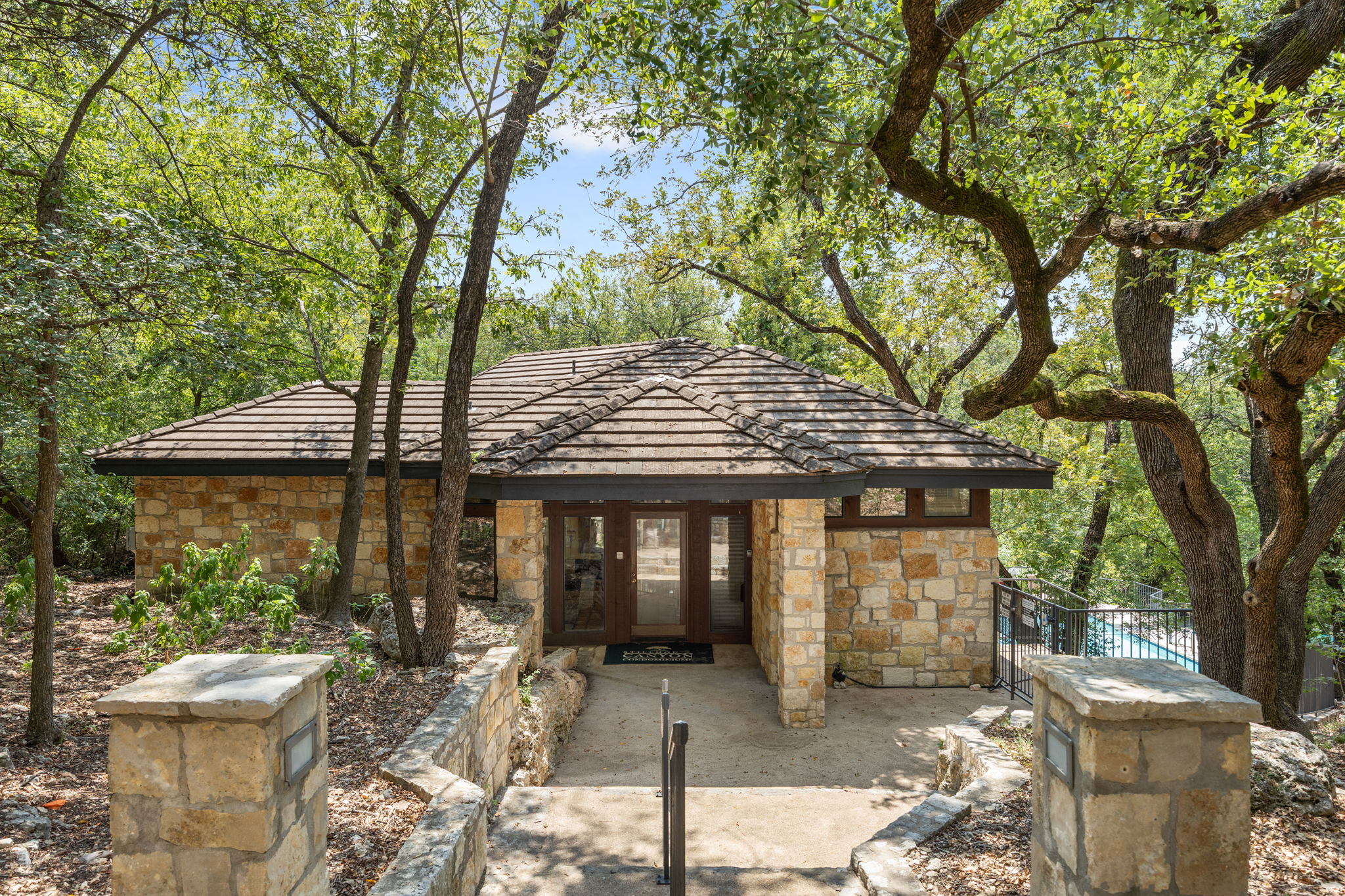 4711 Spicewood Springs Road, Unit 1106 Austin, TX 78759 - Photo 16 of 19 Stone-clad exterior structure featuring a tile roof and prominent mature trees