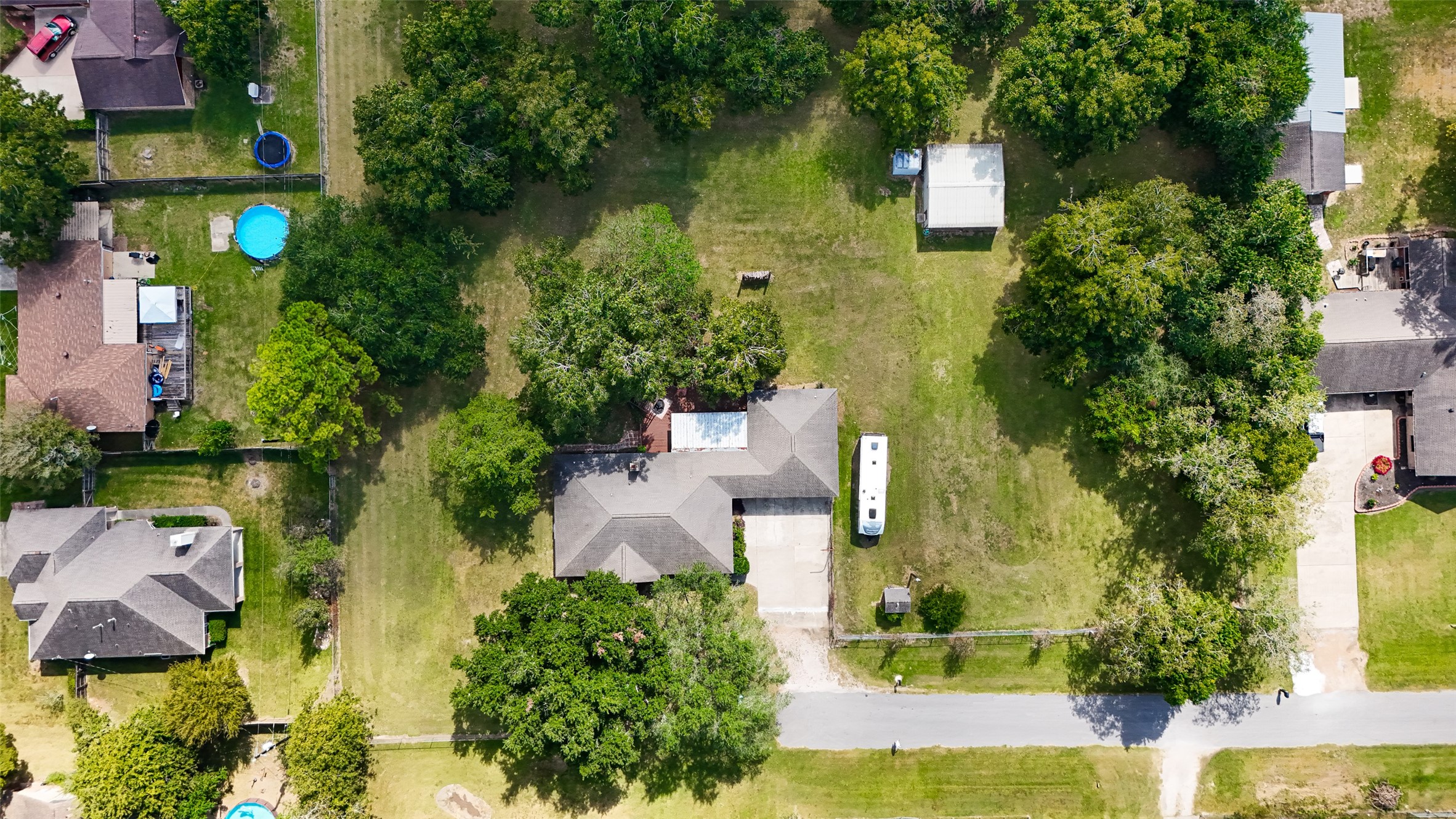 12021 7th 1/2 Street Santa Fe, TX 77510 - Photo 2 of 49 This aerial photo shows a spacious property with a large, well-maintained yard surrounded by mature trees. The house has a sizable driveway and is situated in a quiet, residential neighborhood. There are neighboring homes with pools visible, indicating a family-friendly area.