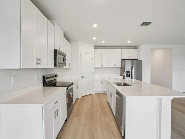 a kitchen with stainless steel appliances a white stove top oven a sink a refrigerator and white cabinets