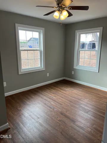 an empty room with wooden floor chandelier fan and windows