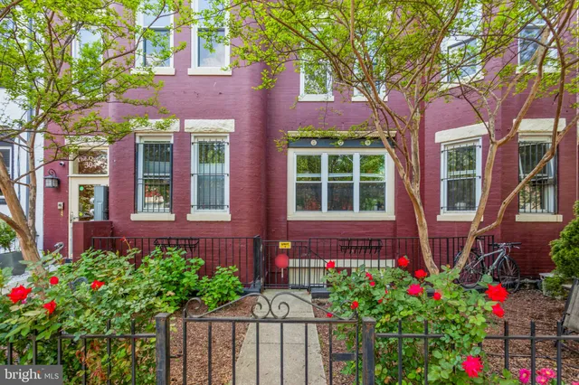 a flower garden is sitting in front of a brick house with large windows