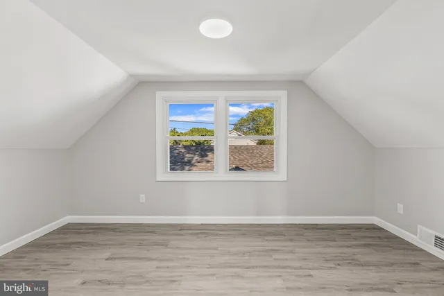 a view of an empty room with window and hardwood floor