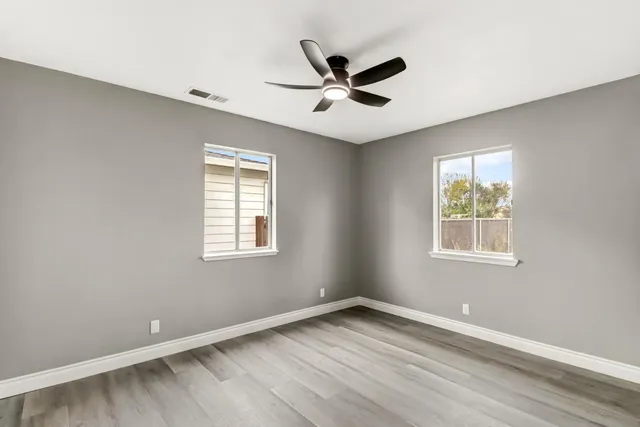 a view of empty room with wooden floor and fan