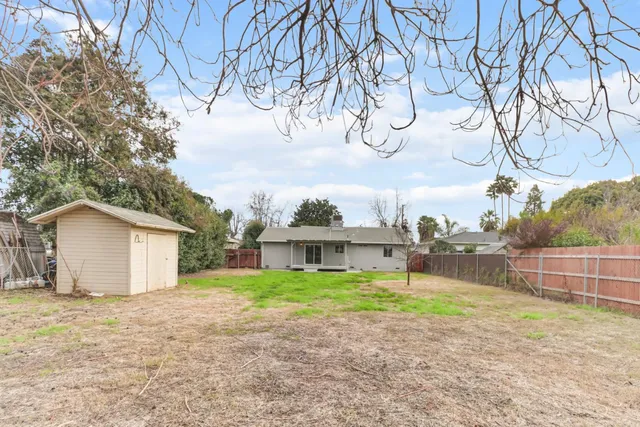 a view of a white house next to a yard with big trees