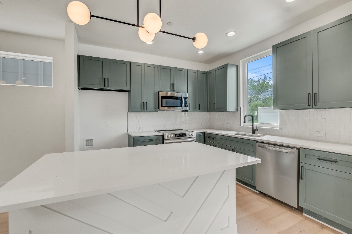 Kitchen featuring appliances with stainless steel finishes, a sink, light wood finished floors, decorative backsplash, and light countertops