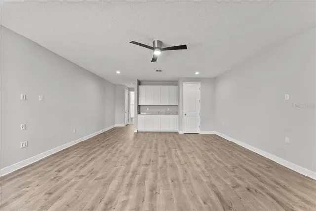 an empty room with wooden floor ceiling fan and windows