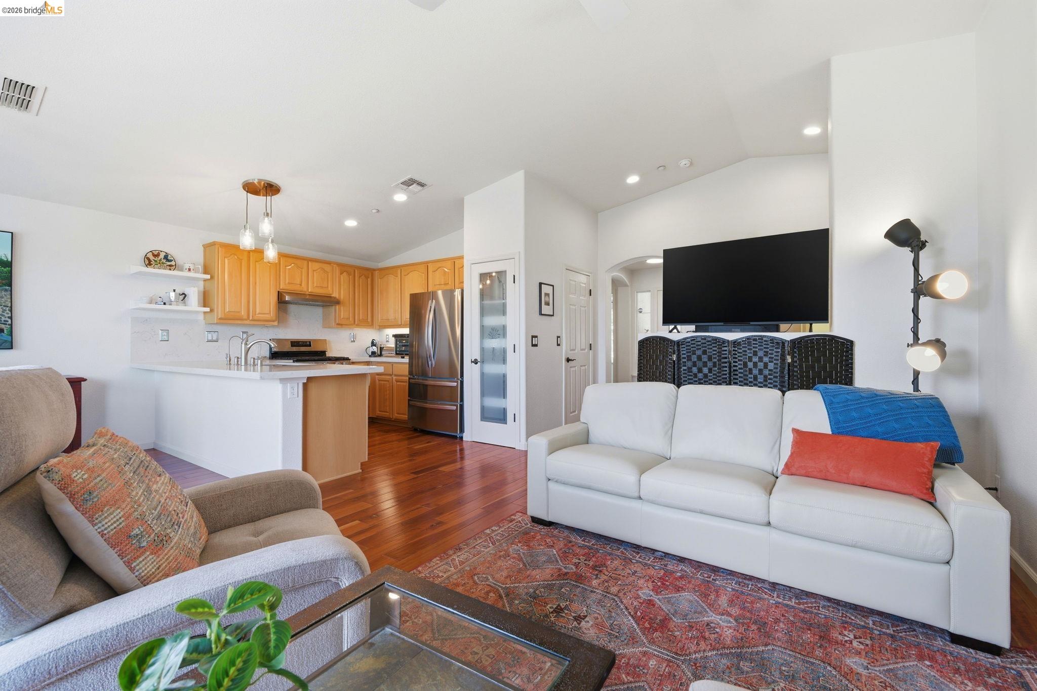 1024 Diamante Rio Vista, CA 94571 - Photo 5 of 27 Open-concept living area featuring rich wood-finish flooring, recessed lighting, vaulted ceiling, a spacious kitchen with light wood cabinetry, and stainless steel appliances