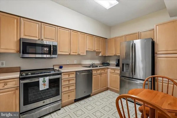 a kitchen with stainless steel appliances a refrigerator a stove a sink dishwasher and white cabinets with wooden floor