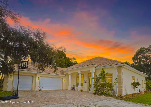 a view of a white house next to a yard with big trees