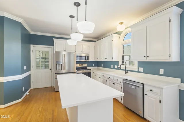 a large kitchen with stainless steel appliances kitchen island granite countertop a stove a sink a refrigerator and white cabinets with wooden floor
