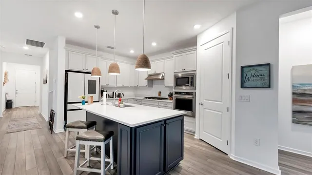 a kitchen with stainless steel appliances kitchen island granite countertop a stove top oven a sink dishwasher and white cabinets with wooden floor