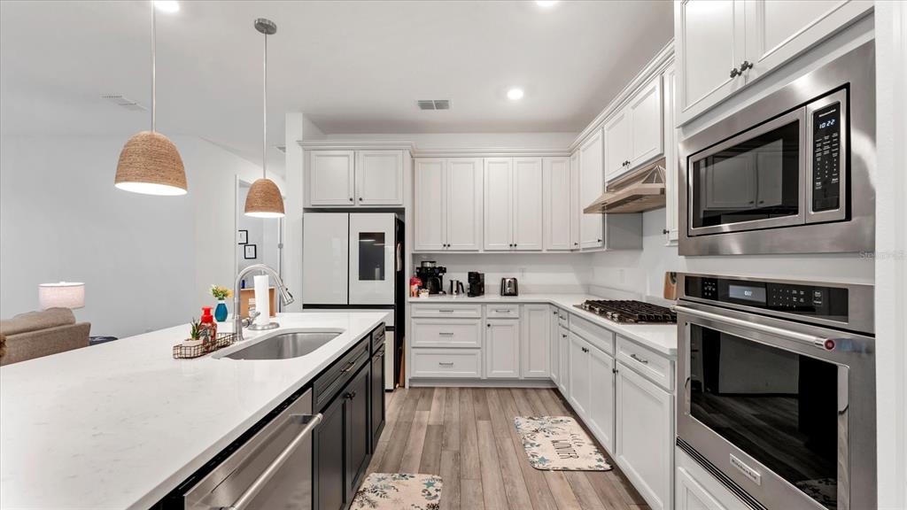 8705 Coastal Key Way Palmetto, FL 34221 - Photo 12 of 64 a kitchen with stainless steel appliances kitchen island granite countertop a stove top oven a sink dishwasher and white cabinets with wooden floor