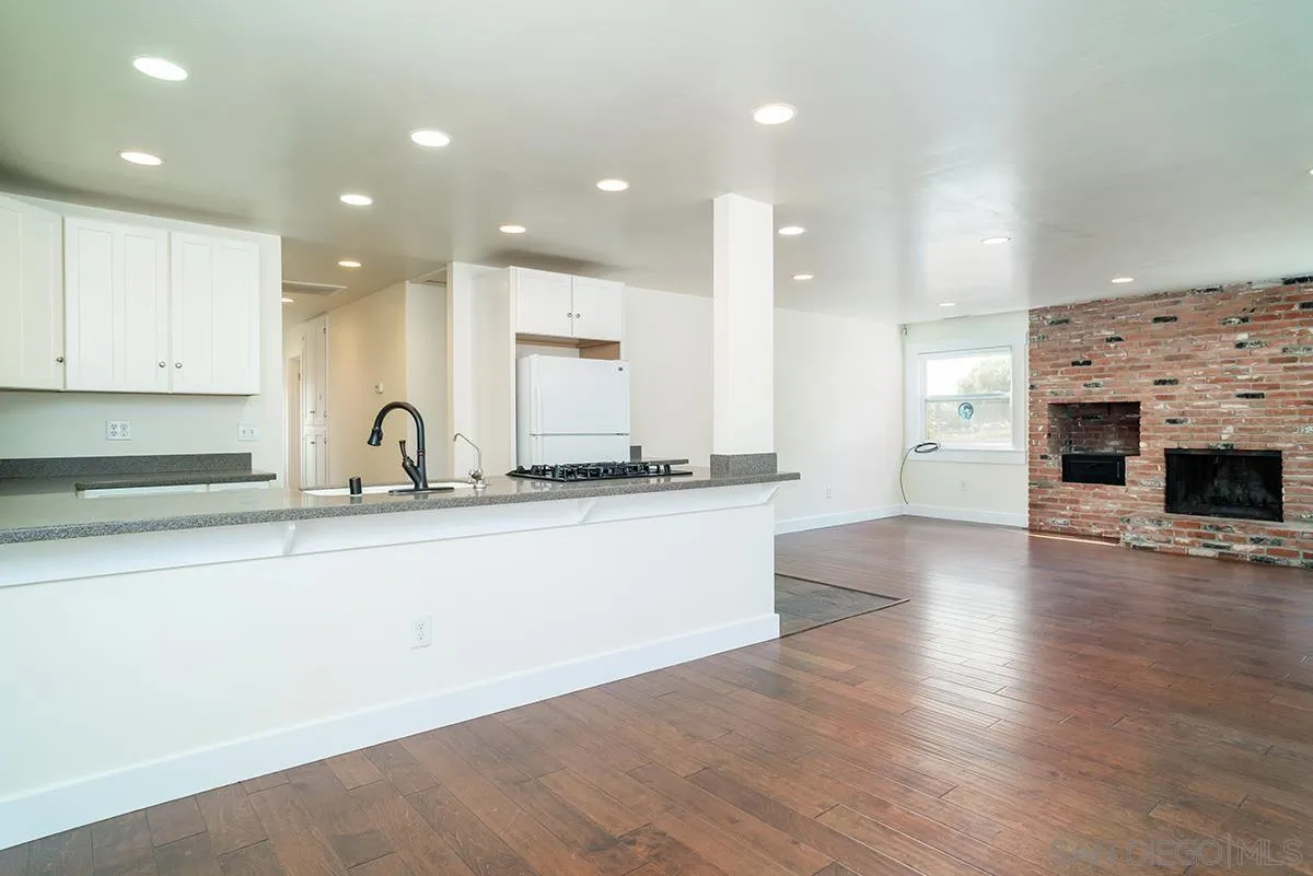 6777 West Lilac Road Bonsall, CA 92003 - Photo 18 of 36 a large kitchen with granite countertop a stove a sink a refrigerator and white cabinets with wooden floor