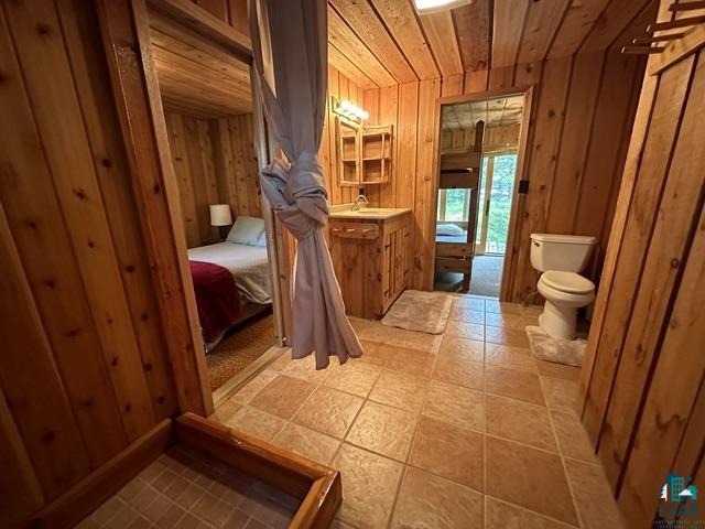 2763 Van Vac Road Ely, MN 55731 - Photo 29 of 37 Wood-paneled bathroom featuring a built-in vanity with a sink, square floor tiles, and a toilet