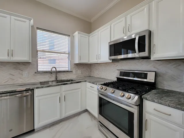 a kitchen with stainless steel appliances granite countertop grey cabinets a stove a sink and dishwasher