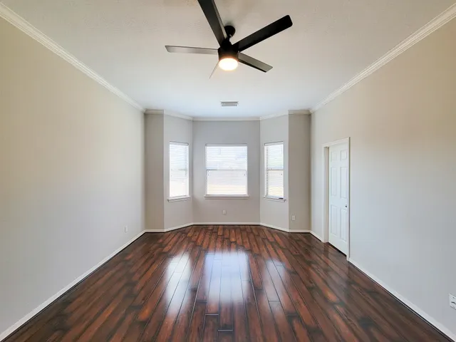 an empty room with wooden floor ceiling fan and windows