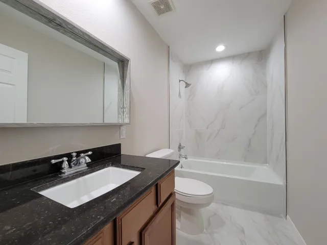a bathroom with a granite countertop sink toilet a mirror and bathtub