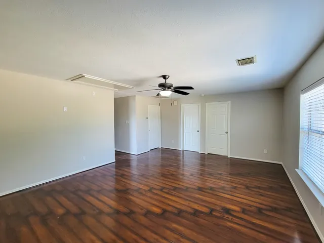 an empty room with wooden floor ceiling fan and windows