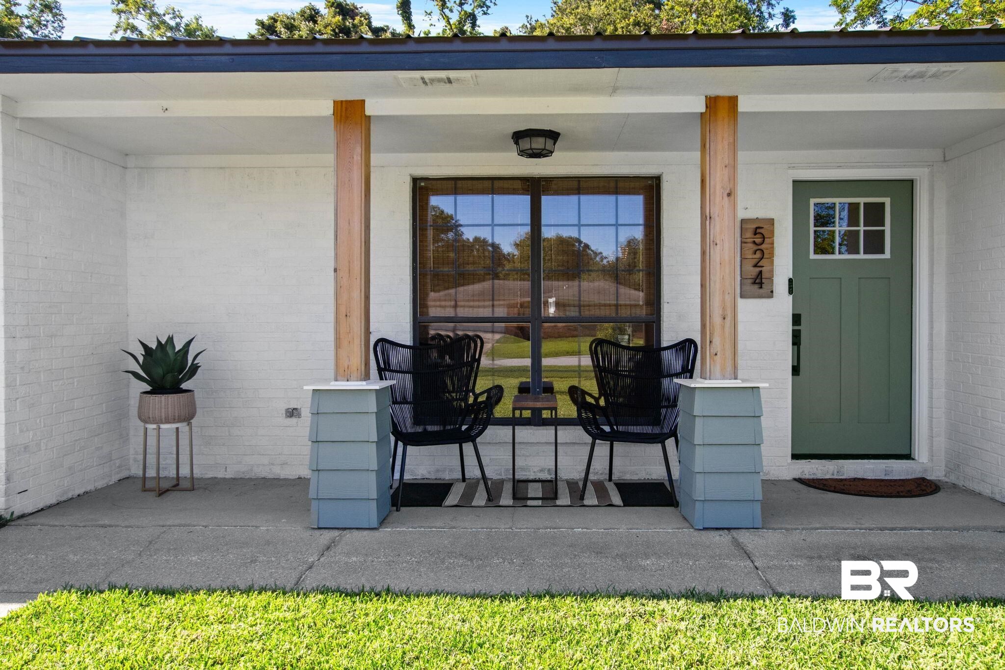 524 Ariel Avenue Foley, AL 36535 - Photo 4 of 37 Covered front porch featuring white painted brick, wood support columns, a green paneled door with windowpanes, a large multi-pane window, and a dark metal outdoor light fixture