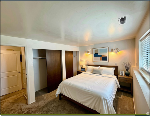 169 East 100 North, Unit B Logan, UT 84321 - Photo 5 of 11 Spacious master bedroom featuring dual wood-panel sliding closet doors, wall-mounted lighting fixtures, a large window with an abundance of light, and neutral-toned wall-to-wall carpeting