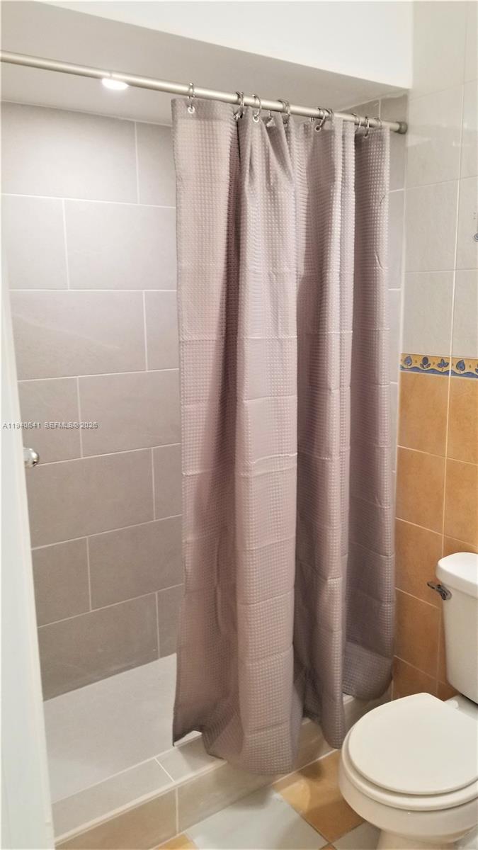9723 Southwest 138th Avenue, Unit IA2L Miami, FL 33186 - Photo 15 of 27 a white toilet sitting next to a shower curtain