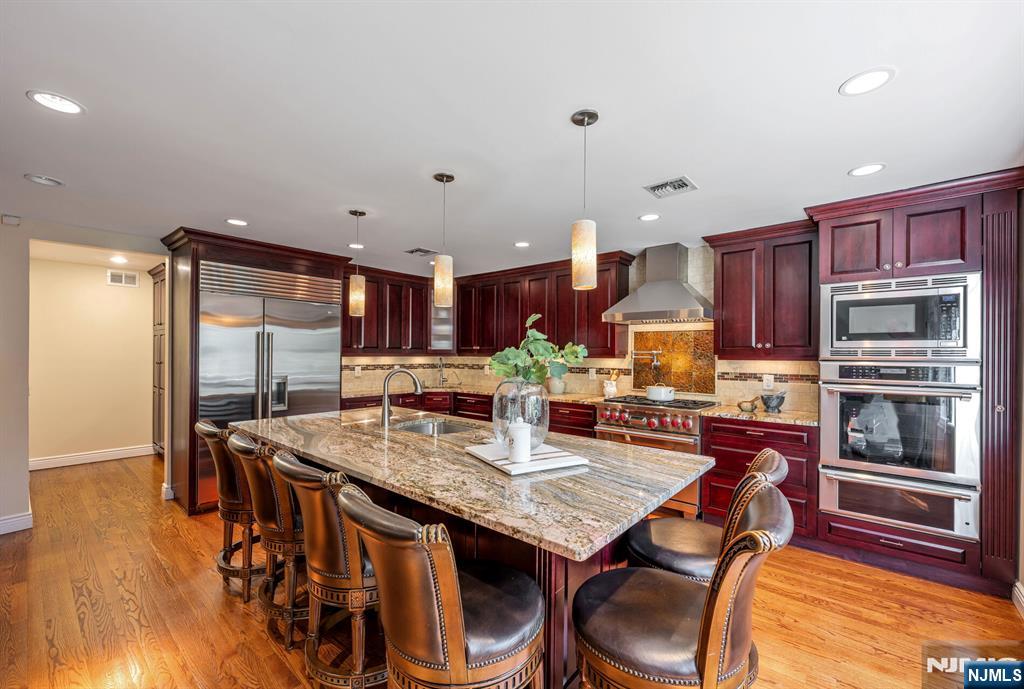 84 Bogerts Mill Road Harrington Park, NJ 07640 - Photo 10 of 47 a kitchen with stainless steel appliances granite countertop a stove a refrigerator a kitchen island a table and chairs with wooden floor