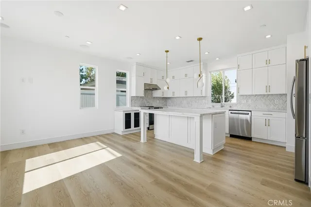 a kitchen with stainless steel appliances kitchen island granite countertop a stove a sink a refrigerator and white cabinets with wooden floor