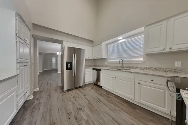 a kitchen with granite countertop a refrigerator a sink dishwasher and white cabinets with wooden floor