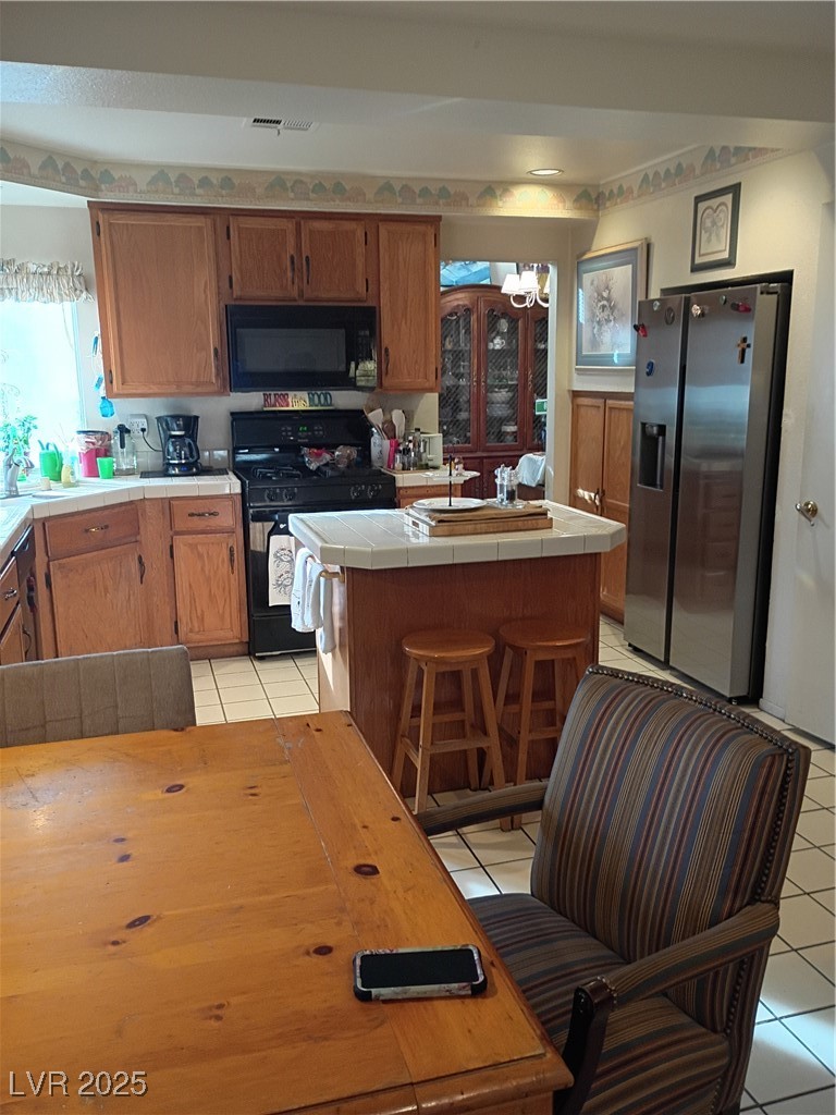 934 Derringer Lane Henderson, NV 89014 - Photo 17 of 49 Kitchen featuring range, refrigerator, light tile patterned flooring, brown cabinets, and a kitchen breakfast bar