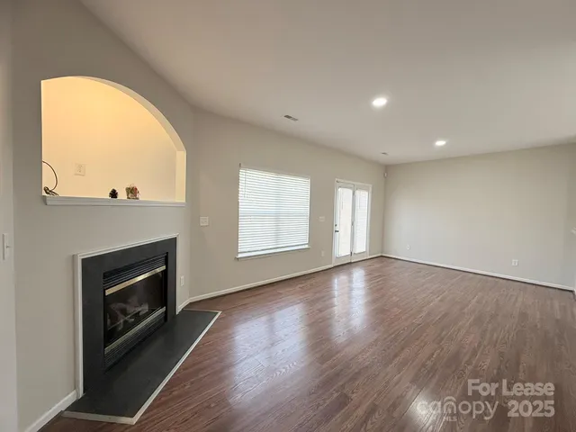 an empty room with wooden floor fireplace and windows