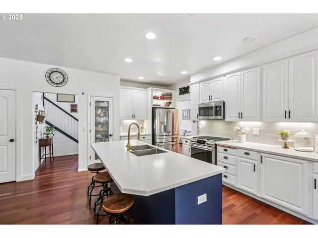 a kitchen with stainless steel appliances kitchen island granite countertop a stove a sink dishwasher and a refrigerator with wooden floor