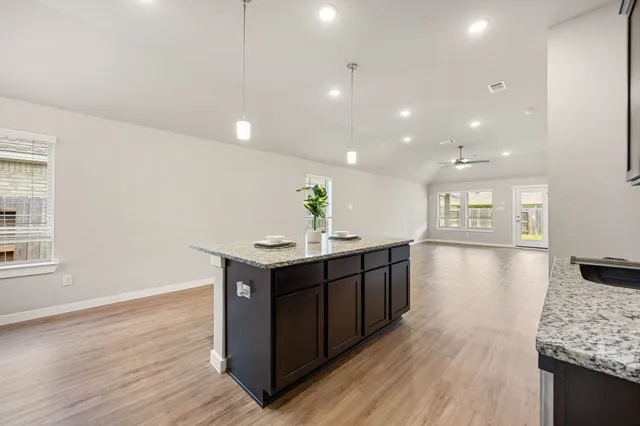 a kitchen with stainless steel appliances granite countertop a sink a stove a refrigerator and a island with wooden floor