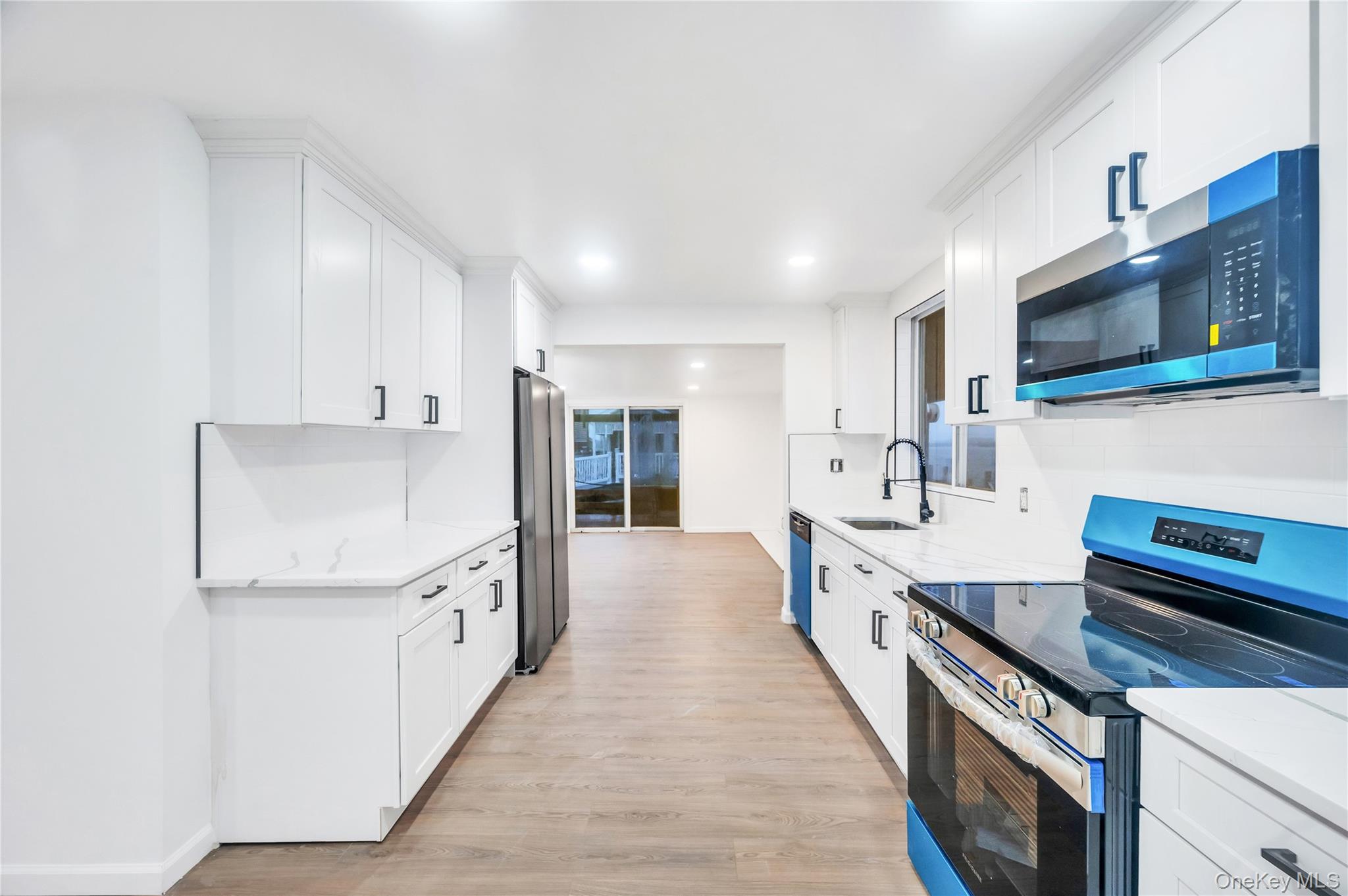 21 Van Brunt Road Queens, NY 11693 - Photo 7 of 17 Kitchen with stainless steel appliances, light wood-style floors, white cabinetry, light stone counters, and recessed lighting