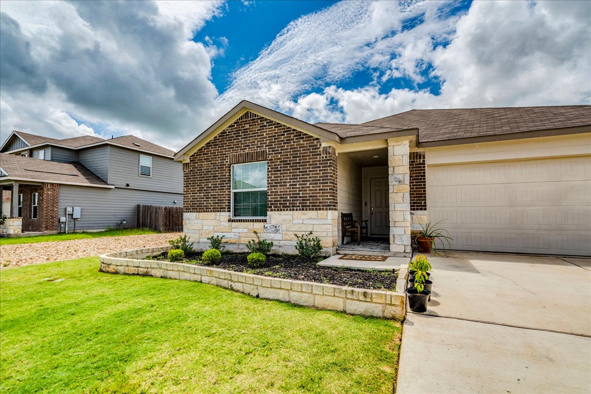 389 Salt Springs Road Kyle, TX 78640 - Photo 6 of 30 A welcoming facade with a stone and brick exterior, a paved driveway, and vibrant green lawn.