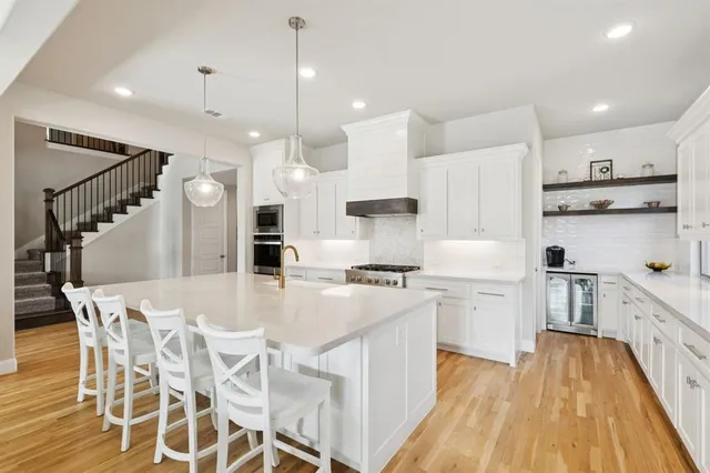 a large kitchen with stainless steel appliances kitchen island granite countertop a stove a sink a refrigerator and white cabinets with wooden floor