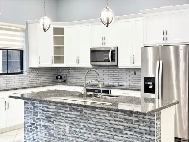 a kitchen with stainless steel appliances kitchen island granite countertop a sink refrigerator stove and microwave