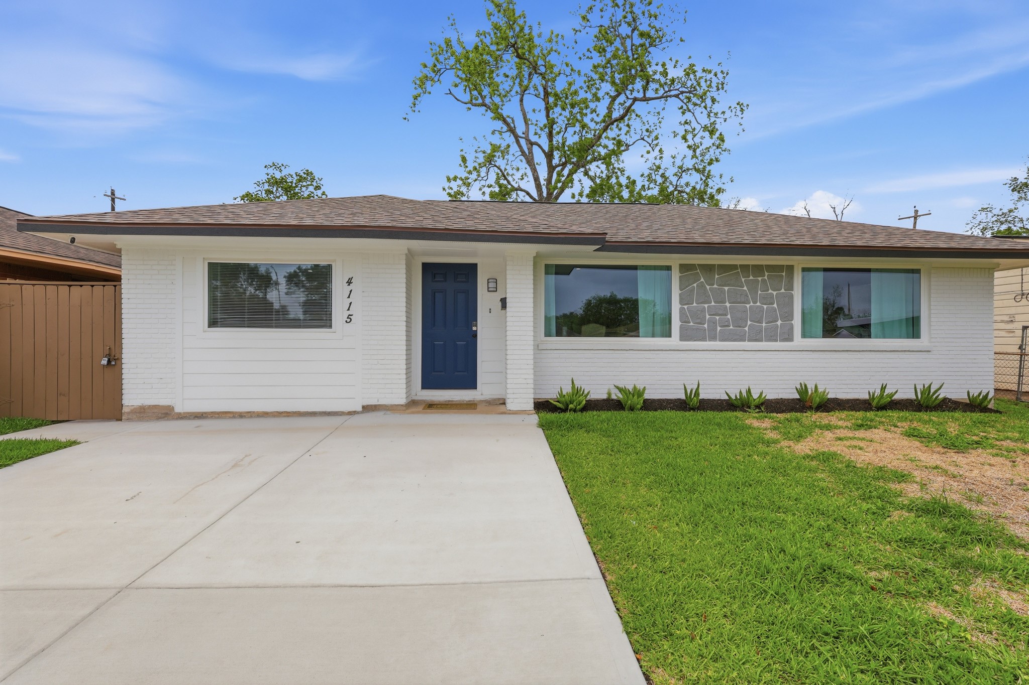 This charming home features a clean, modern exterior with fresh white brick and a contrasting blue front door. It has a spacious driveway, well-maintained lawn, and tasteful landscaping for great curb appeal.
