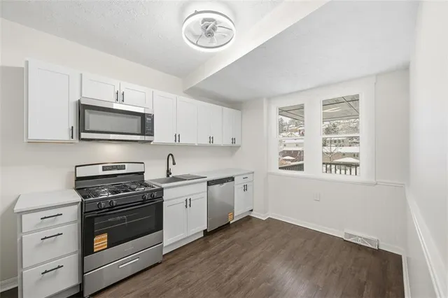 a kitchen with stainless steel appliances granite countertop white cabinets a sink a stove a refrigerator and dishwasher with wooden floor