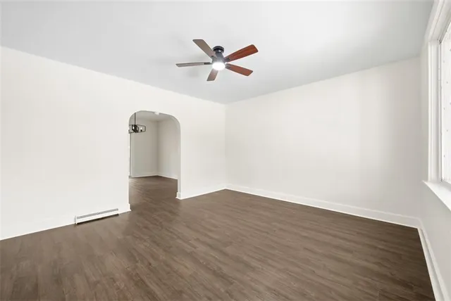 an empty room with wooden floor fan and windows