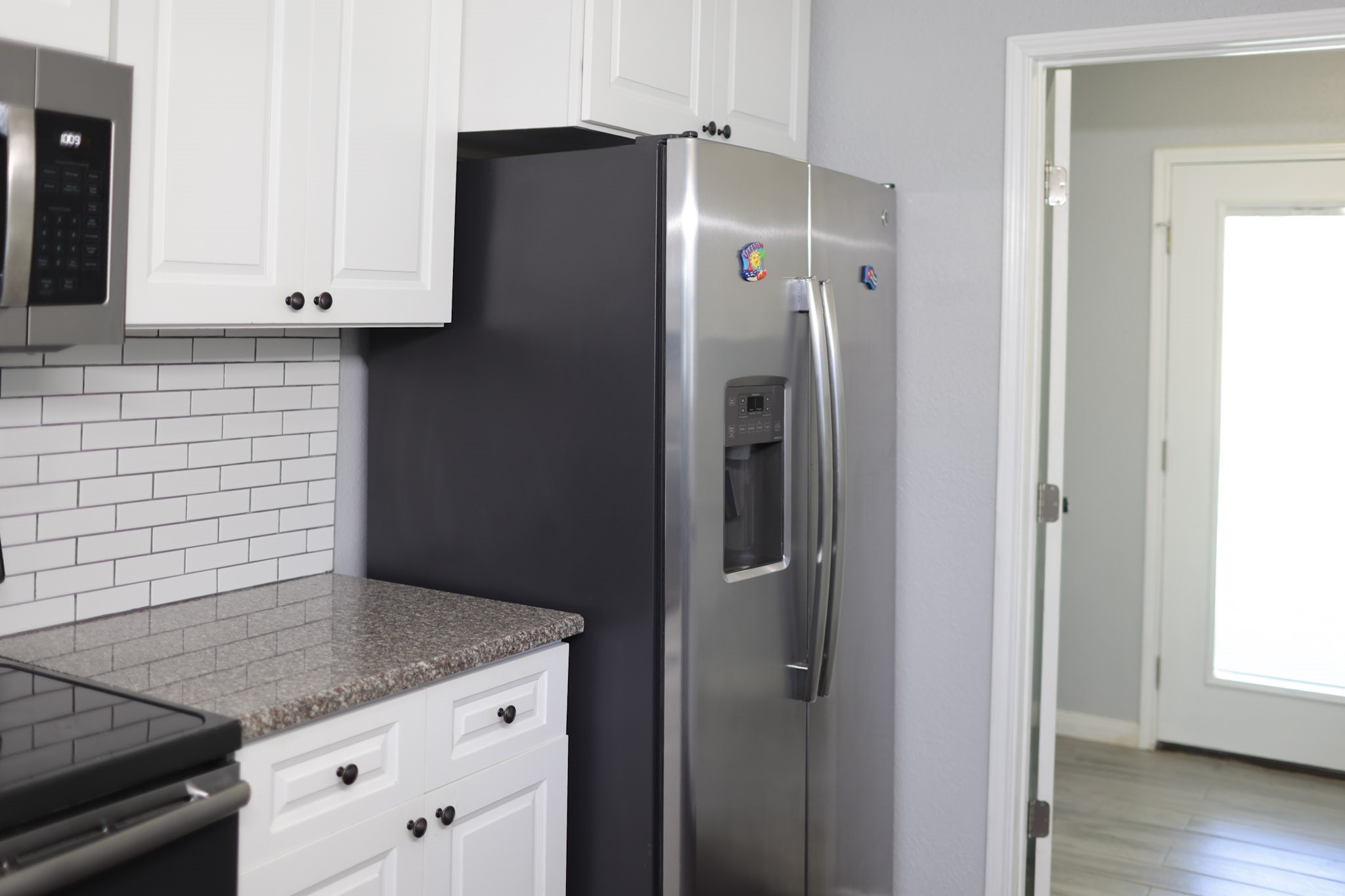 407 Tamarind Street Lake Jackson, TX 77566 - Photo 18 of 36 Modern kitchen featuring a sleek stainless steel refrigerator, white cabinetry, and a classic subway tile backsplash. Bright and inviting space with a granite countertop and ample storage.