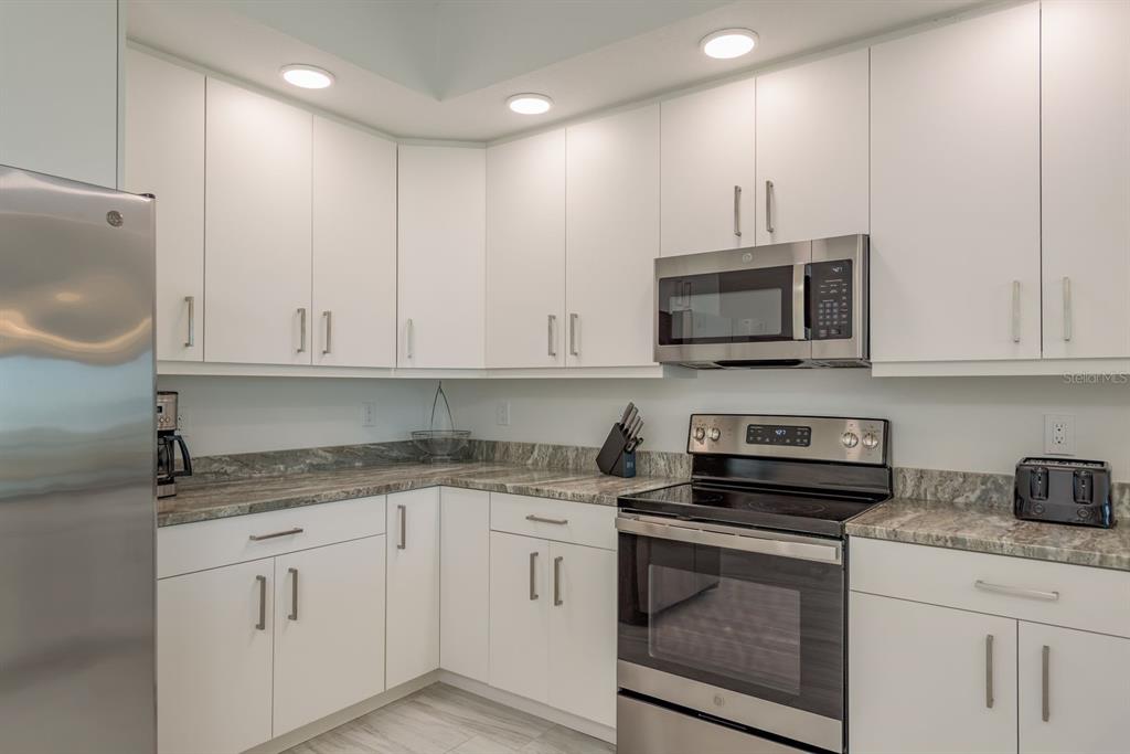 415 Island Way, Unit 402 Clearwater Beach, FL 33767 - Photo 12 of 35 a kitchen with granite countertop white cabinets white stainless steel appliances and a sink